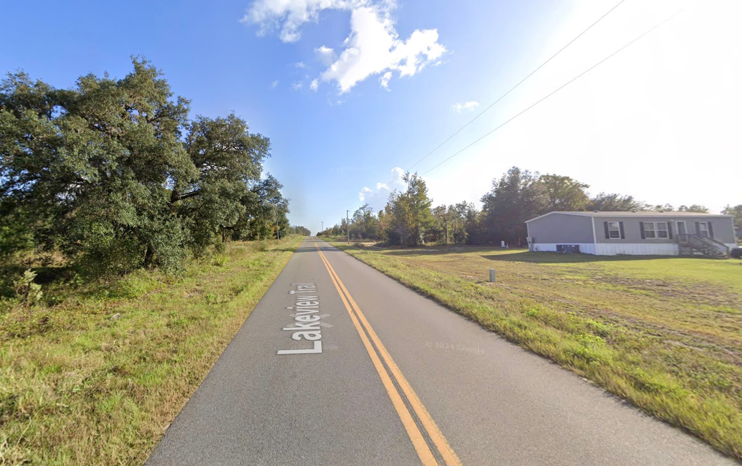 Paved rural road with yellow center line running through open land dotted with trees in Putnam County, Florida.