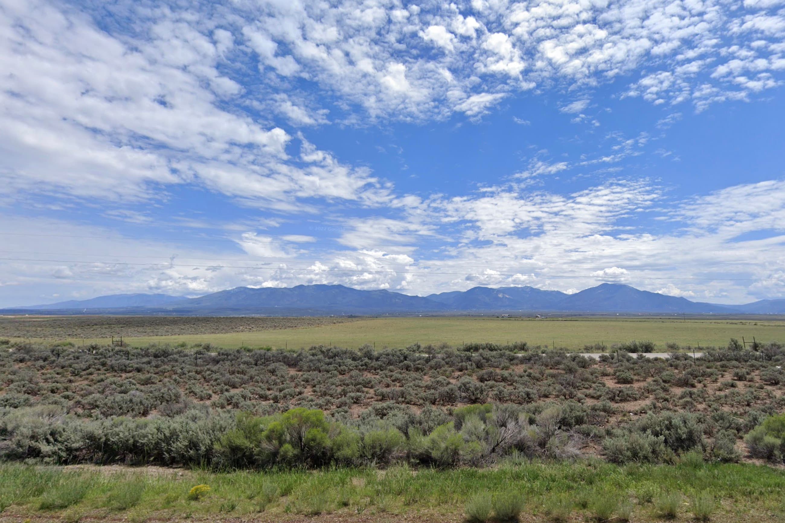 Open grassland with sagebrush vegetation and mountains visible along the horizon in Taos County, New Mexico.