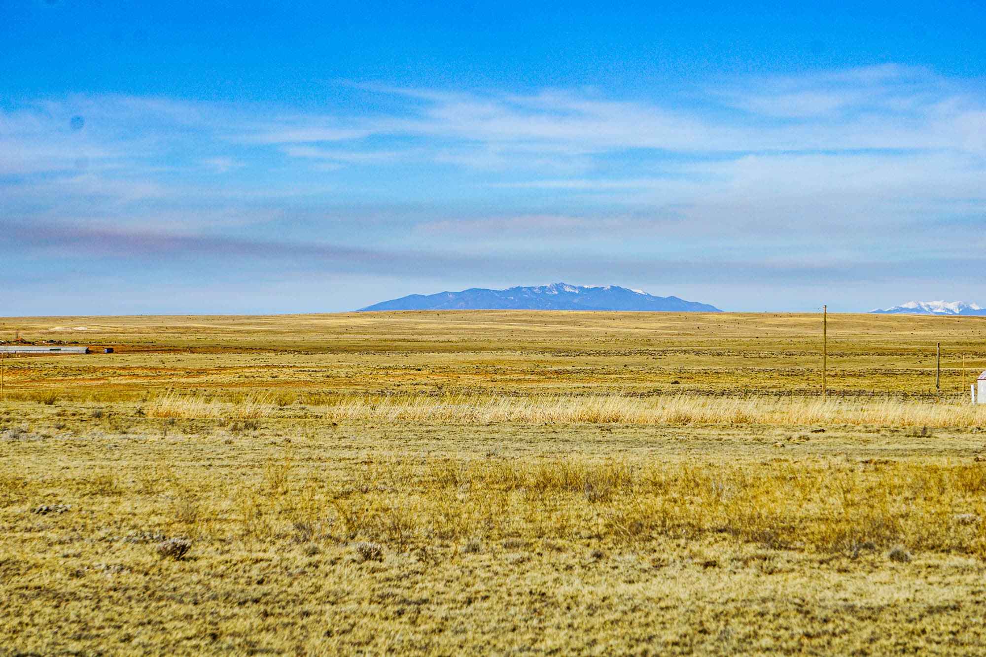 Snow-capped Manzano Mountains visible across flat grassland near Estancia Ranchettes in Torrance County, New Mexico.