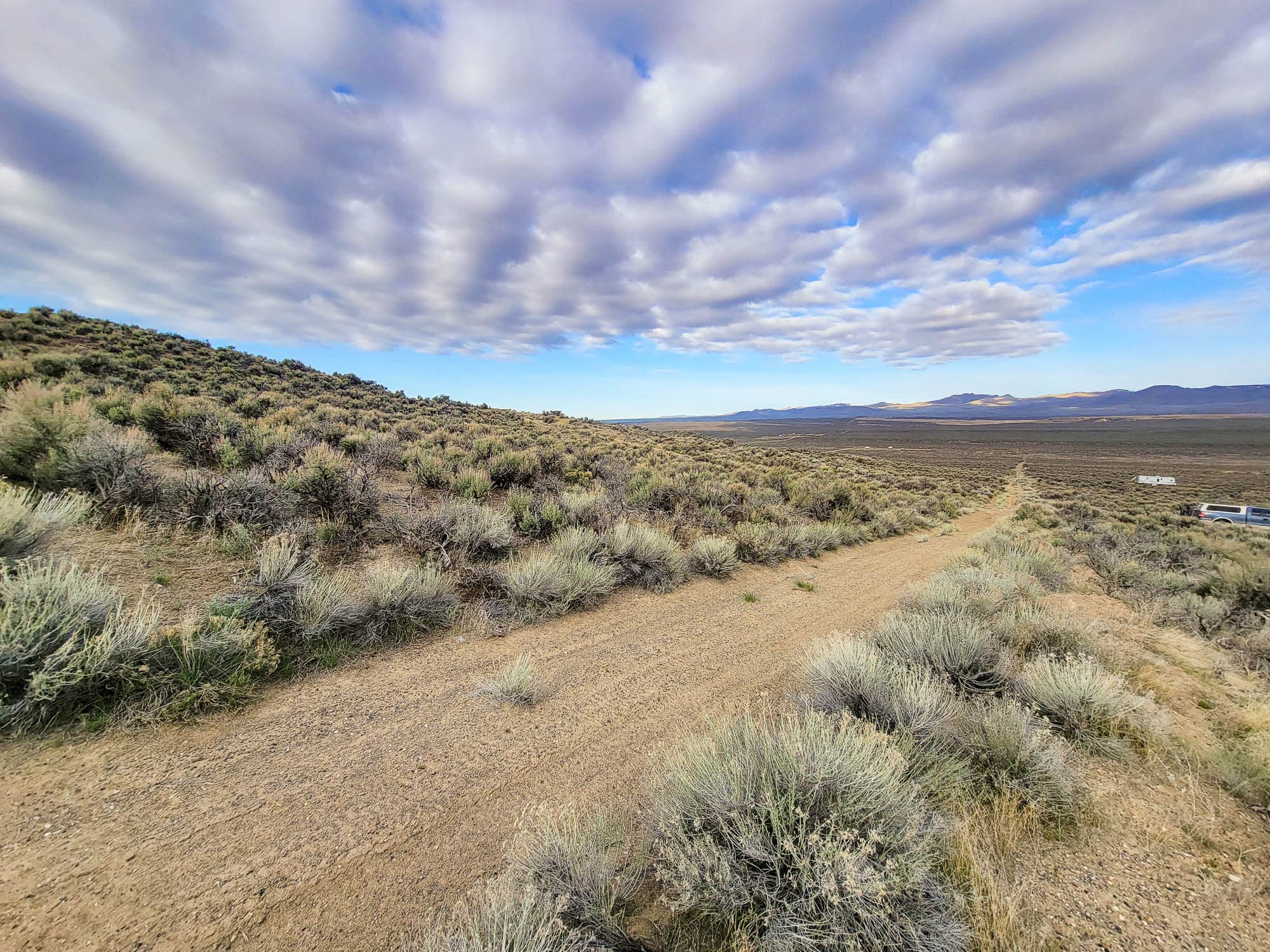 A dirt two-track running along a sage ridge and dropping toward a wide valley, banded cloud stretched across the sky.