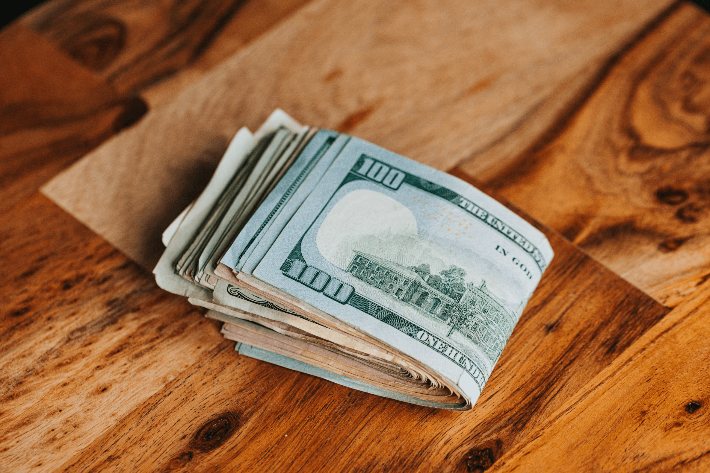 A folded stack of twenty and hundred dollar bills sitting on a brown envelope on a wooden table.