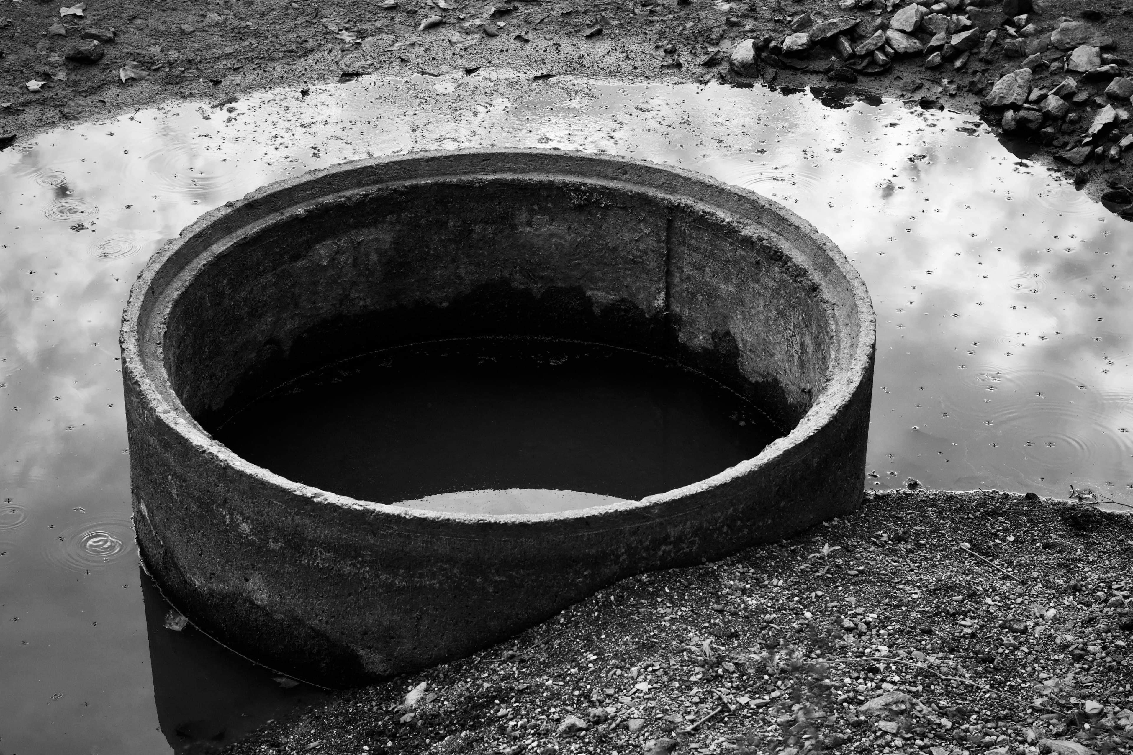 A large precast concrete tank ring sitting in gravel, photographed in black and white.