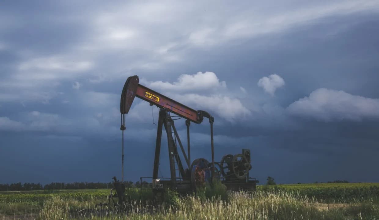 An oil pumpjack standing in a green field under a heavy grey sky.