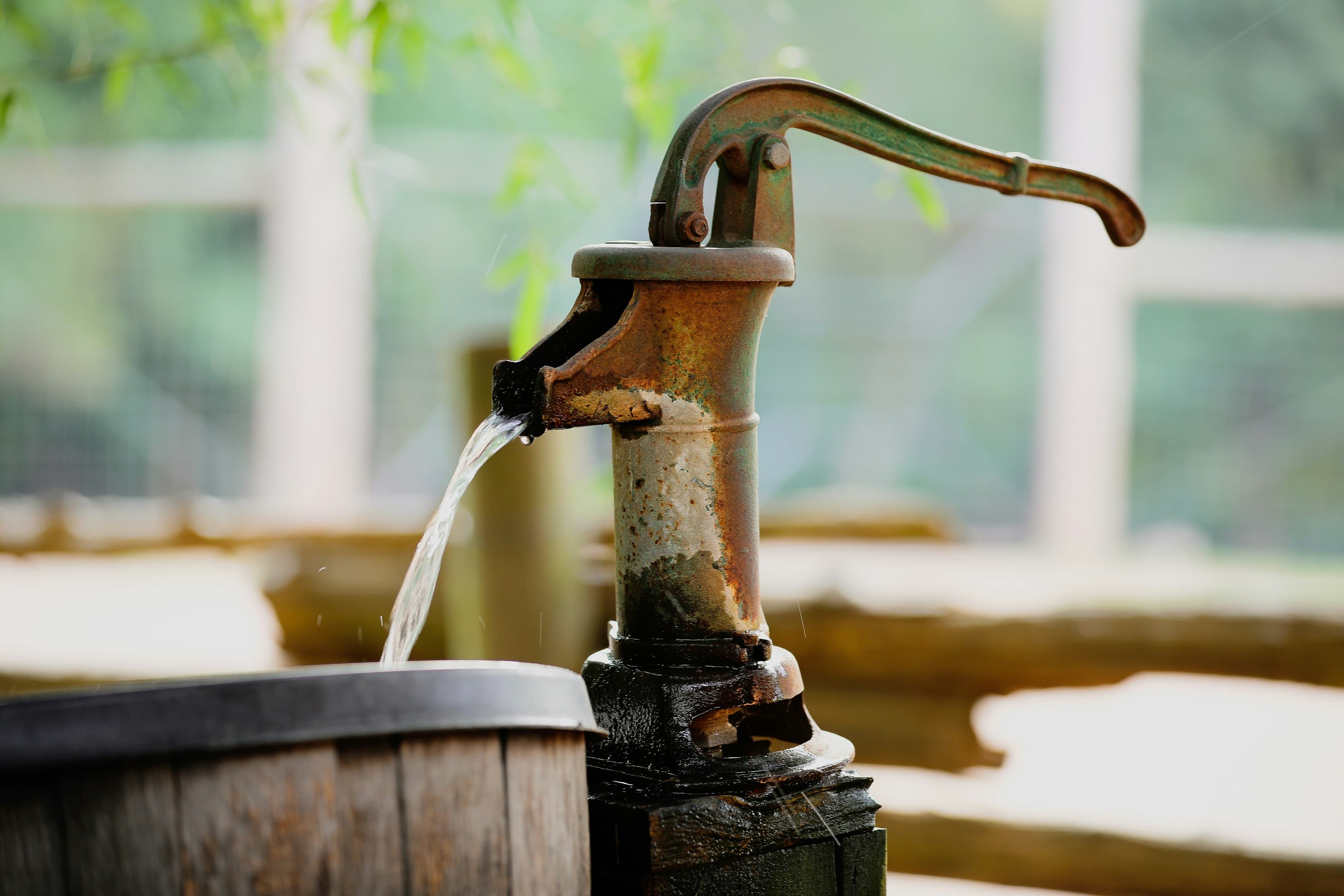 An old cast iron hand pump pouring a steady stream of water into a wooden barrel.