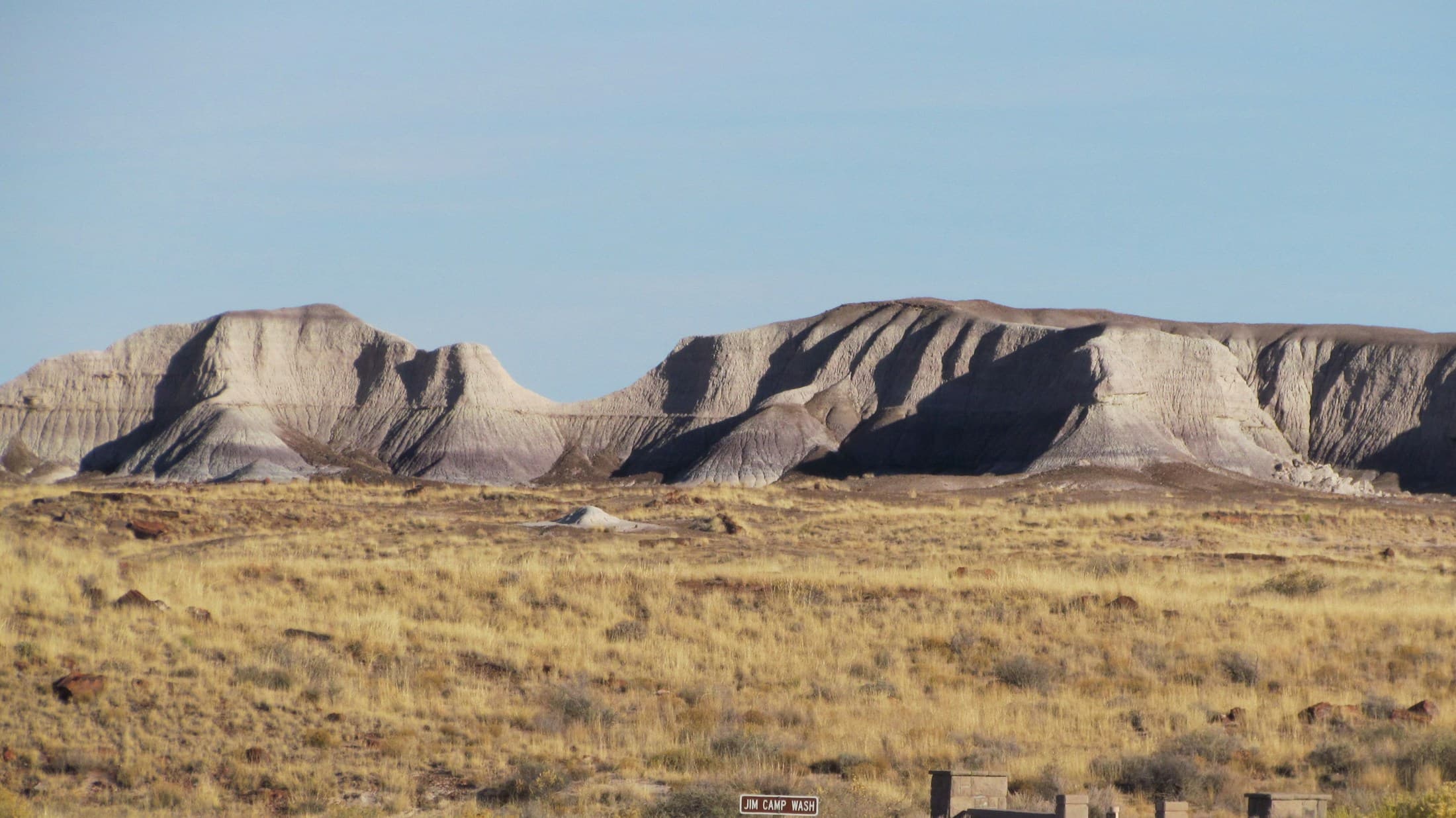 Pale grassland running flat to a line of low banded mesas under a wide clear sky.