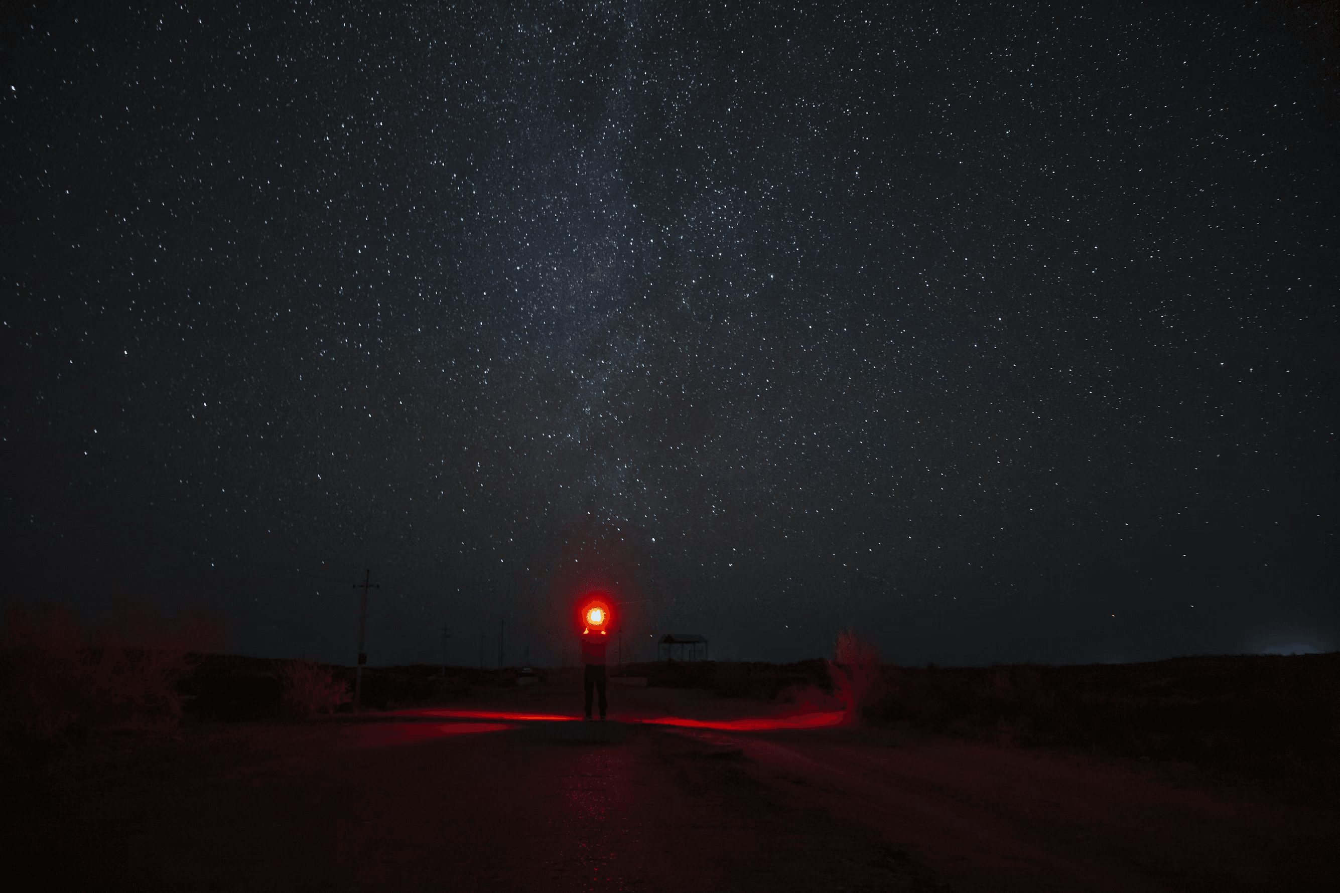 A person on a dirt road under the Milky Way, lit by a red headlamp