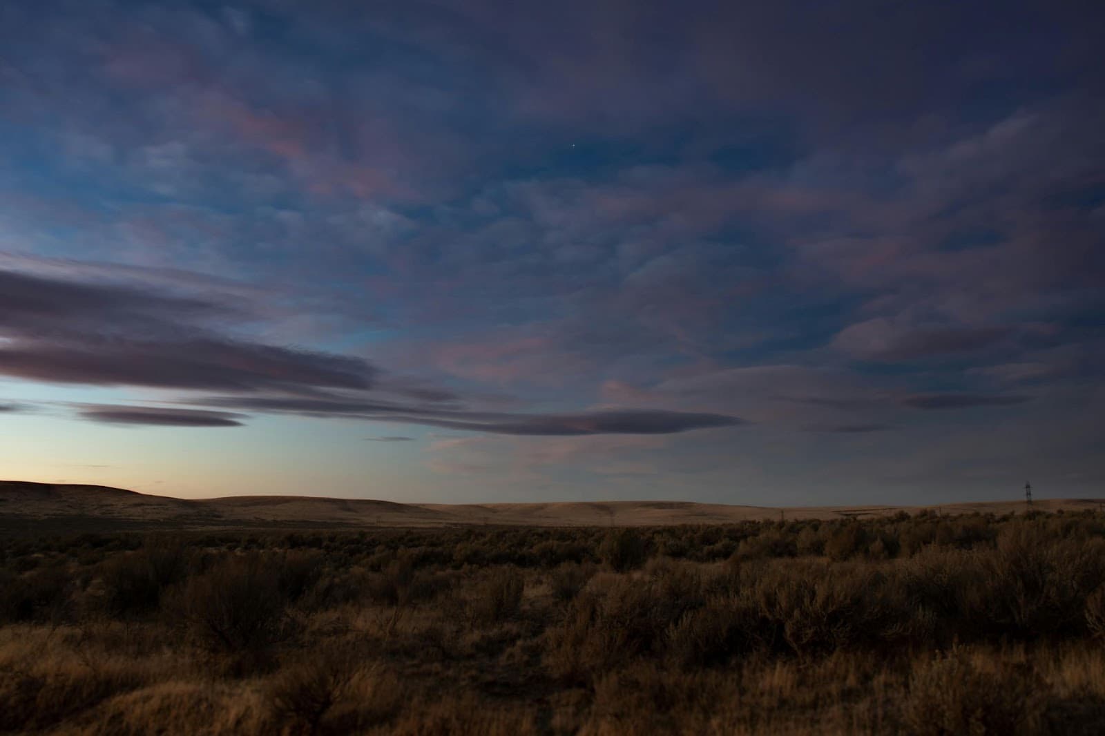 Sagebrush plain under a wide dusk sky streaked with lavender cloud, low hills on the far horizon.
